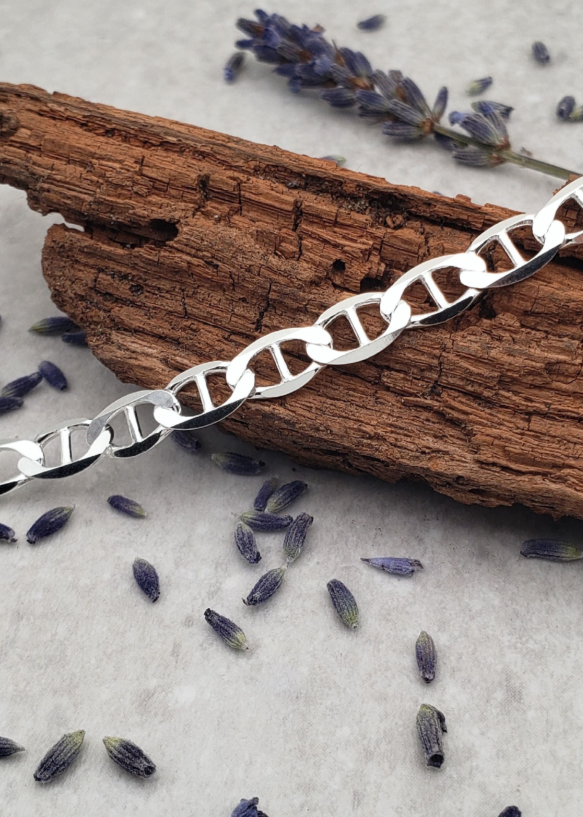 A chain bracelet artfully placed on wood, with bits of lavendar scattered