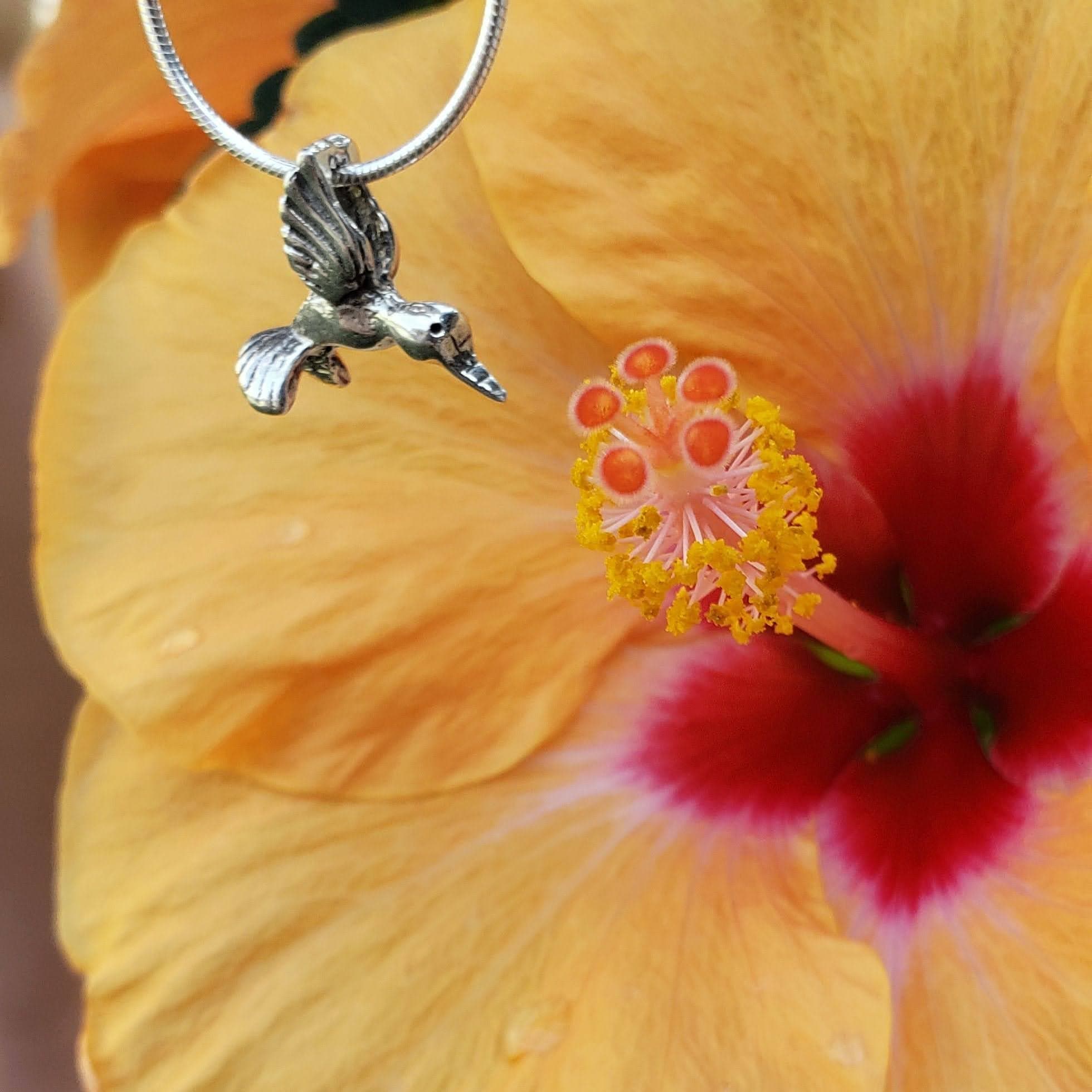 A hummingbird pendant hanging over a flower as if about to drink from it